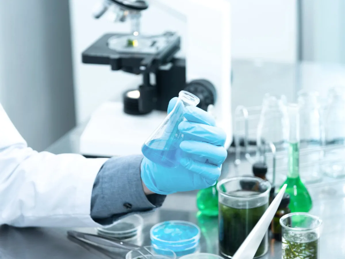 Gloved hand working with lab glassware beside a microscope